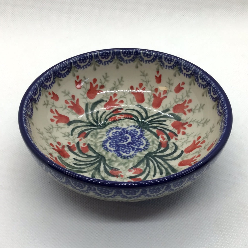 A ceramic shallow bowl with a floral pattern, featuring a central red and blue floral motif surrounded by a green and red leafy border on a white background.